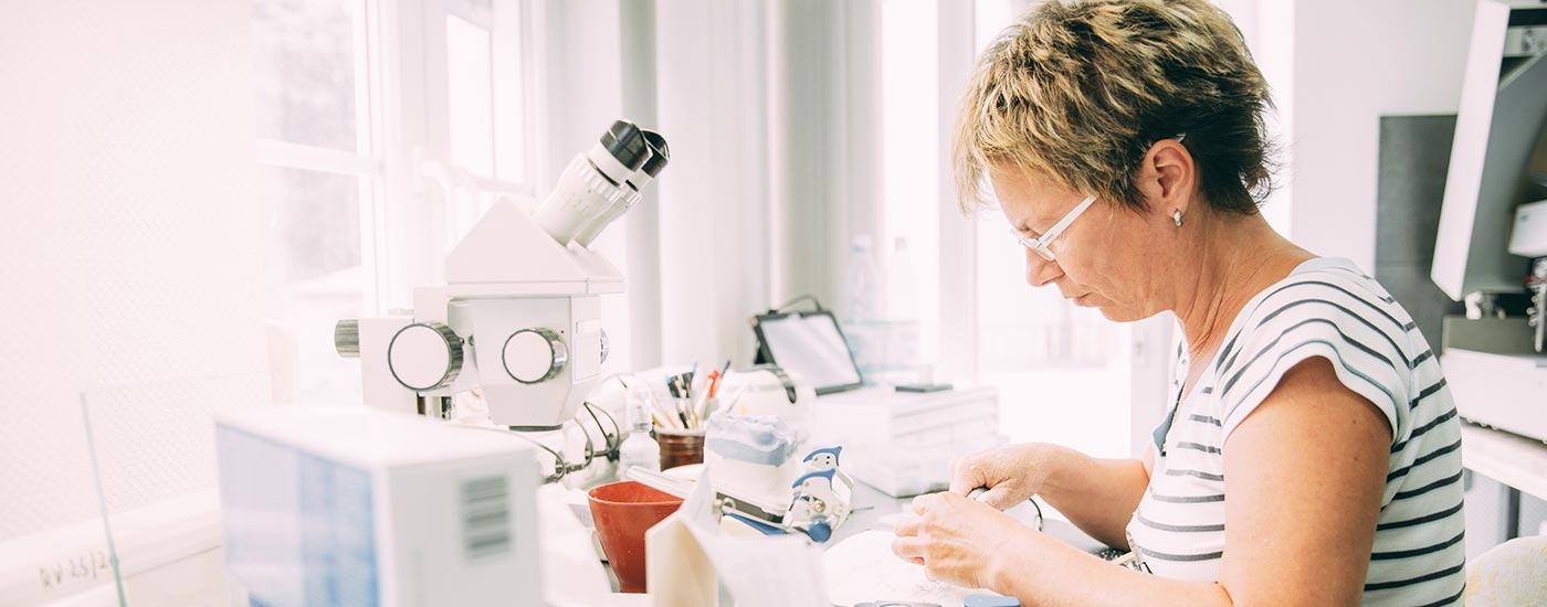 Eine Zahntechnikerin mit kurzem Haar und Brille fertigt ästhetischen Zahnersatz im Labor der Praxis zahn-B.
