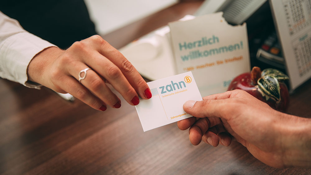 Eine Hand in Großaufnahme überreicht eine Visitenkarte der Zahnarztpraxis zahn-B in Strausberg