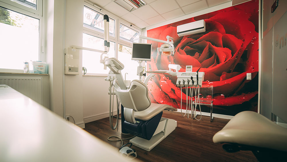 Vom Behandlungsstuhl dieses Raums aus genießen Patienten den Blick auf eine wandfüllende Rosentapete in leuchtendem Rot.